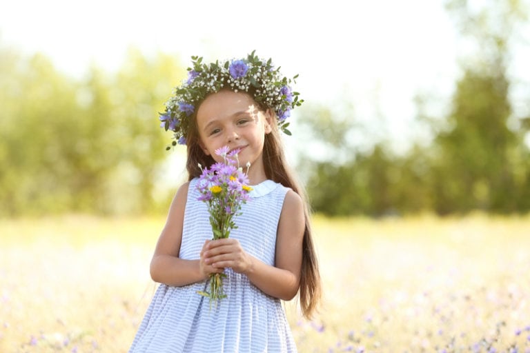 kleines Mädchen mit einer Blumenkrone auf dem Kopf, das draußen mit einem Blumenstrauß steht