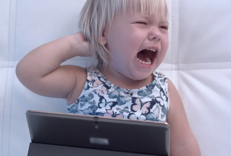 Weinendes Baby mit digitalem Tablet, das auf dem Sofa sitzt