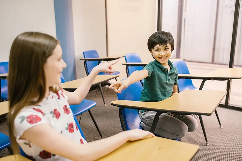 zwei fröhliche Kinder, die im Klassenzimmer aufeinander zeigen