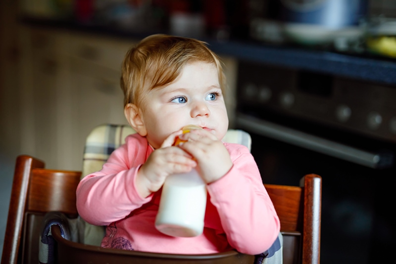 ein Baby, das die Babyflasche hält, während es im Fütterstuhl sitzt