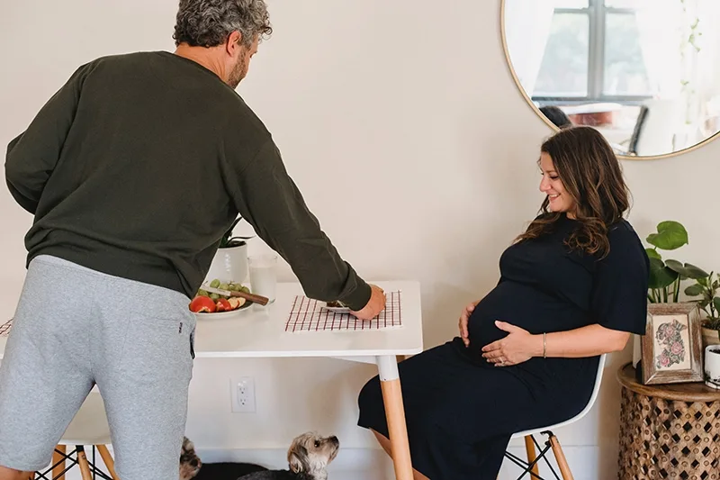 ein Ehemann, der seiner am Tisch sitzenden schwangeren Frau Essen serviert