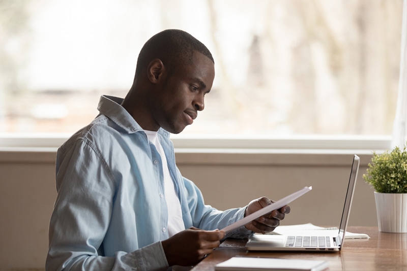 ein Mann liest einen Brief, während er zu Hause vor dem Laptop sitzt