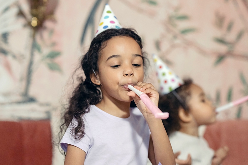 ein kleines Mädchen feiert Geburtstag und bläst Partypfeife