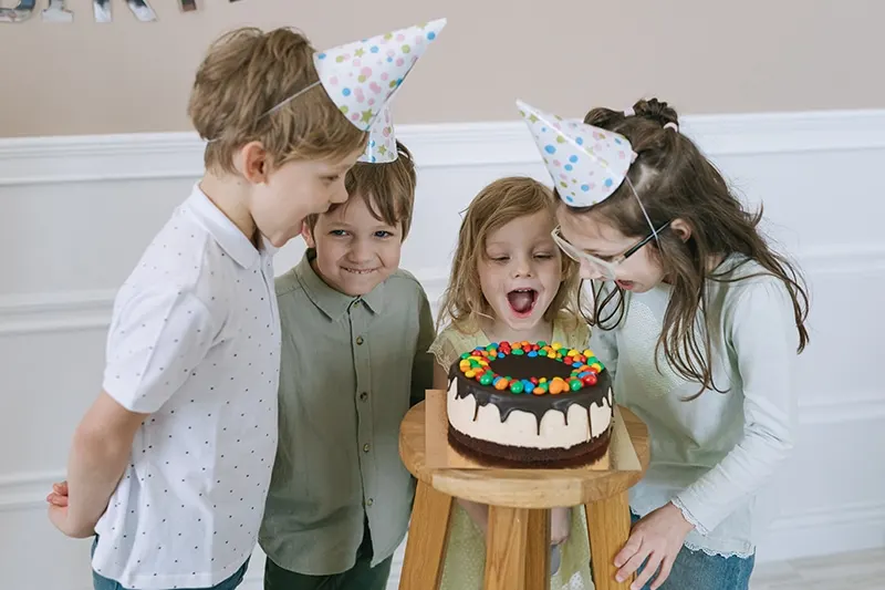 eine Gruppe von Kindern, die den Geburtstagskuchen betrachten und sich glücklich fühlen
