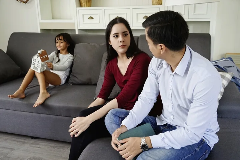 geschiedene Eltern unterhalten sich vor ihrer Tochter, während sie im Wohnzimmer sitzen
