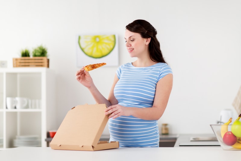 glückliche schwangere frau, die pizza isst