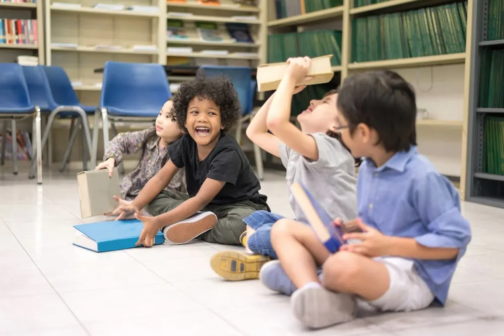 glückliche Kinder, die mit Büchern spielen, die im Klassenzimmer auf dem Boden sitzen
