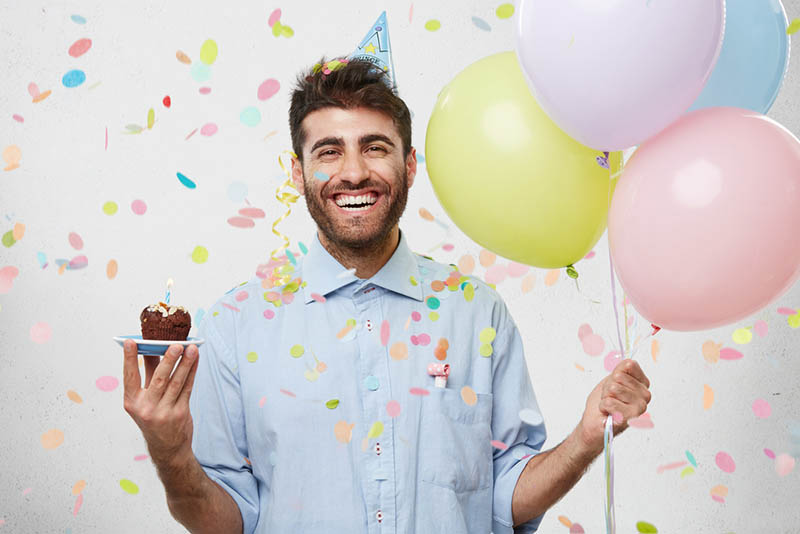 glücklicher Mann feiert Geburtstag mit Luftballons und einem Mini-Kuchen
