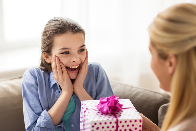 glückliches Mädchen, das zu Hause ein Geburtstagsgeschenk von der Mutter erhält