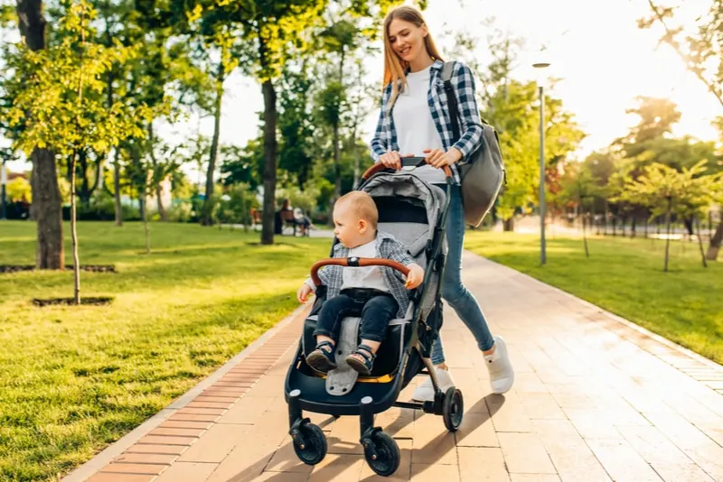 junge Mutter geht mit einem kleinen Kleinkind im Kinderwagen spazieren