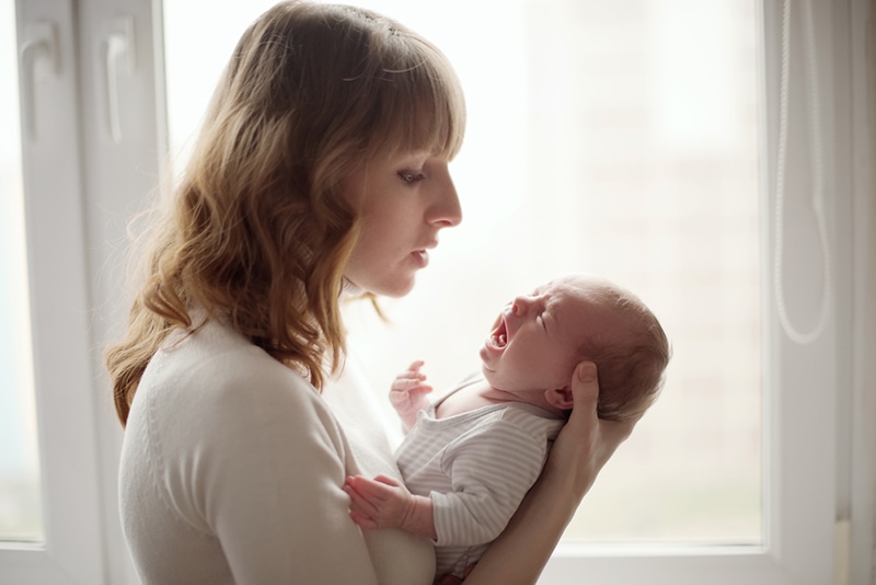 junge Mutter, die ein weinendes Baby tröstet, während sie es in den Armen hält