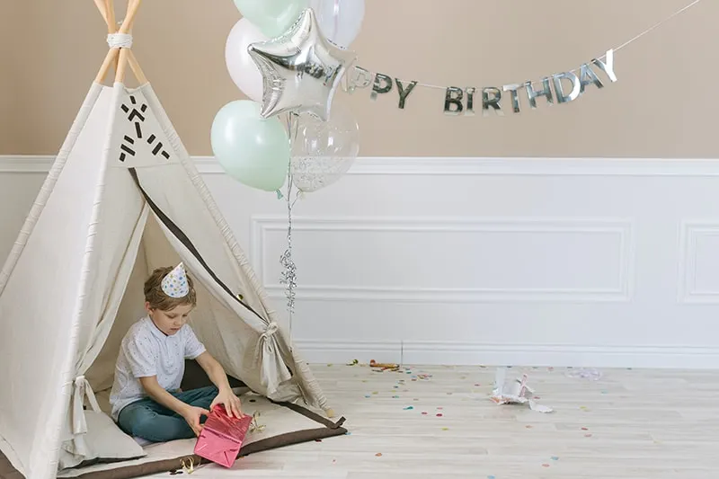 kleiner Junge öffnet ein Geburtstagsgeschenk, während er in einem Zelt sitzt