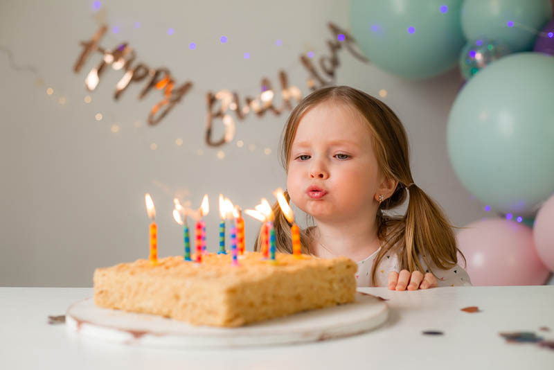 kleines Mädchen bläst eine Kerze auf ihrem Geburtstagskuchen aus