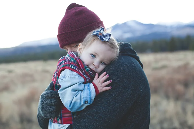 kleines Mädchen, das sich auf die Schulter ihres Vaters stützt, während er sie in den Armen hält