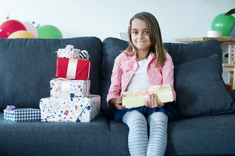 kleines Mädchen mit Geburtstagsgeschenk auf der Couch sitzend
