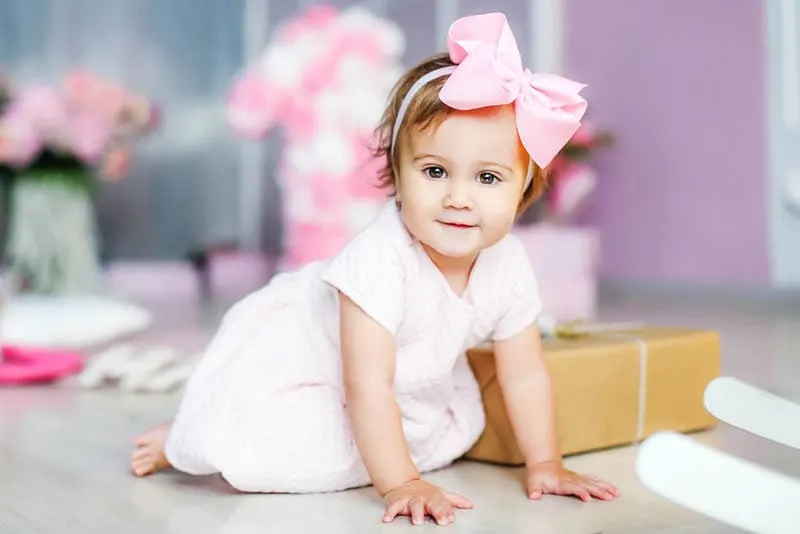 kleines Mädchen mit großen rosa Schleife auf dem Kopf sitzt auf dem Boden mit Geschenk