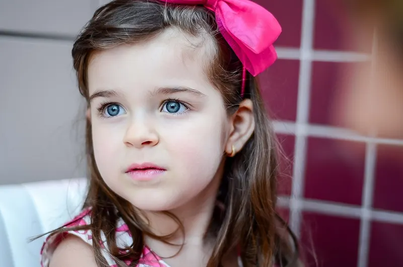 kleines Mädchen mit rosa Schleife im Haar, das beiseite schaut