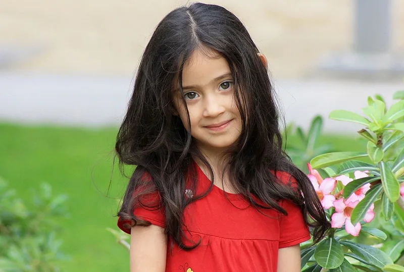 kleines Mädchen mit schwarzen Haaren, das in der Nähe der Blumen im Garten steht