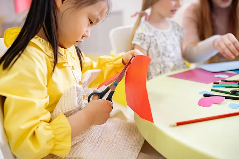 kleines Mädchen schneidet Papier mit einer Schere am Tisch