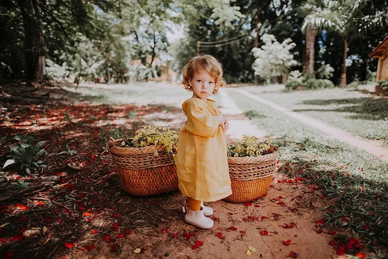 kleines Mädchen steht unter dem Baum in der Nähe von Körben voller Blumen