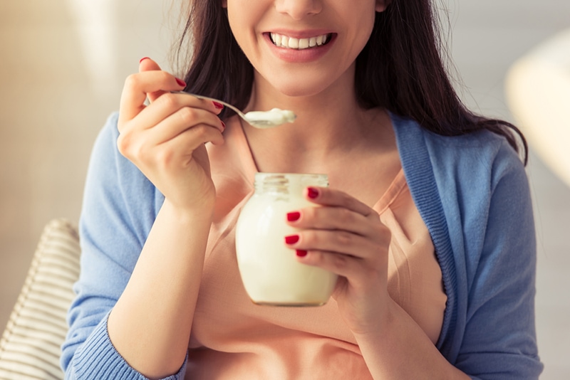 lächelnde Frau isst Joghurt aus dem Glas