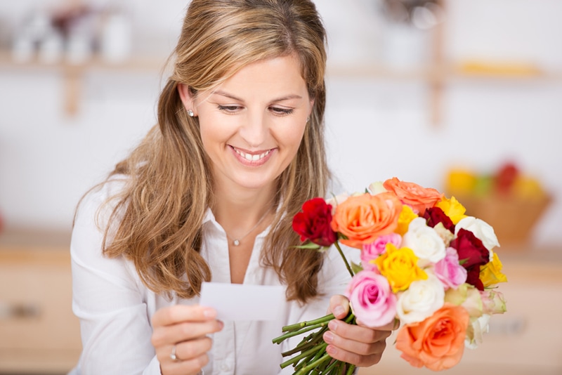 lächelnde Frau, die eine Grußkarte liest und einen Blumenstrauß hält