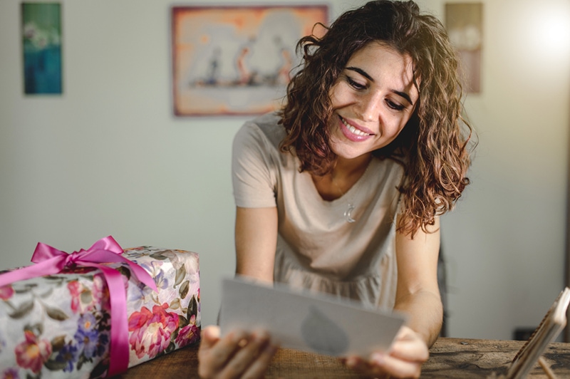 lächelnde Frau liest Geburtstagskarte, nachdem sie ein Geschenk erhalten hat