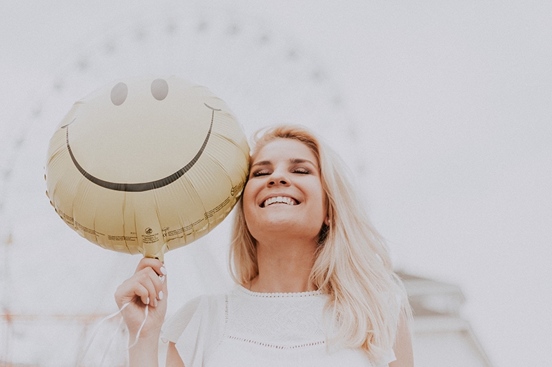 lächelnde Frau mit gelbem Ballon mit Smiley-Gesicht