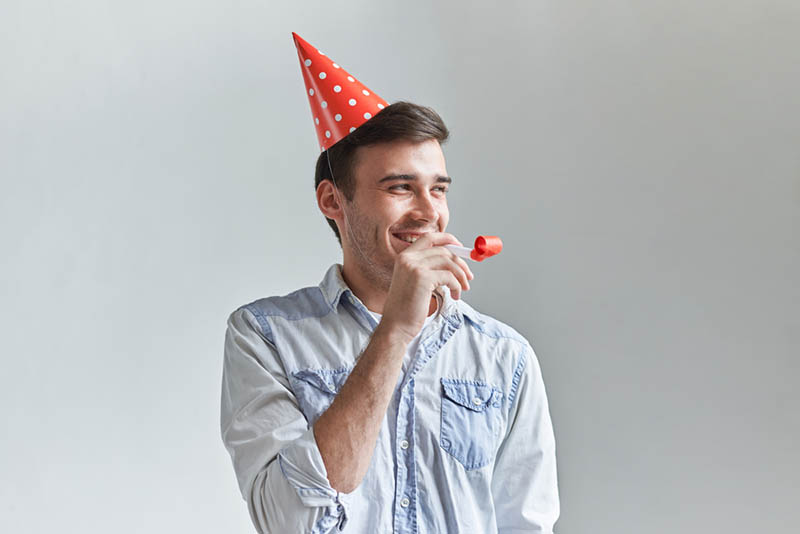 lächelnder Mann feiert Geburtstag mit Party-Pfeife