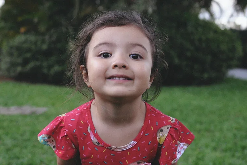 lächelndes kleines Mädchen im roten Kleid, das im Park steht