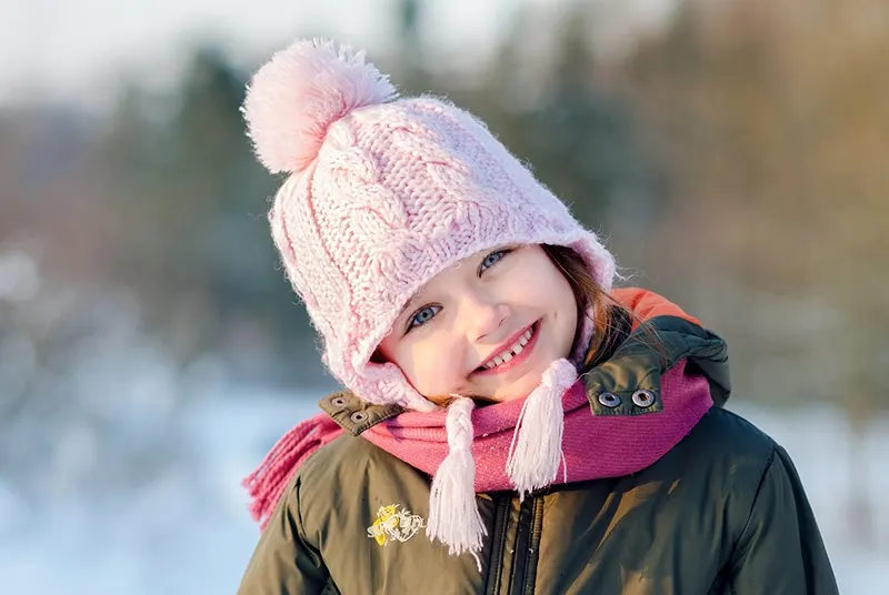 lächelndes kleines Mädchen mit rosa Strickmütze und grüner Jacke