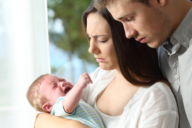 müde Eltern, die weinendes Baby betrachten, während sie es in den Armen halten