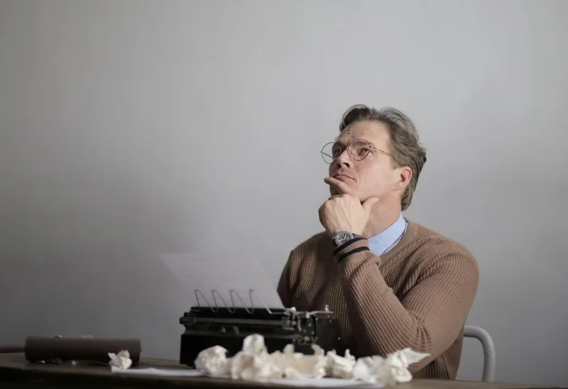nachdenklicher Mann, der aufschaut, während er vor der Schreibmaschine sitzt