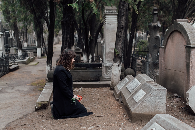 traurige Frau, die neben dem Grab kniet und Blumen hält