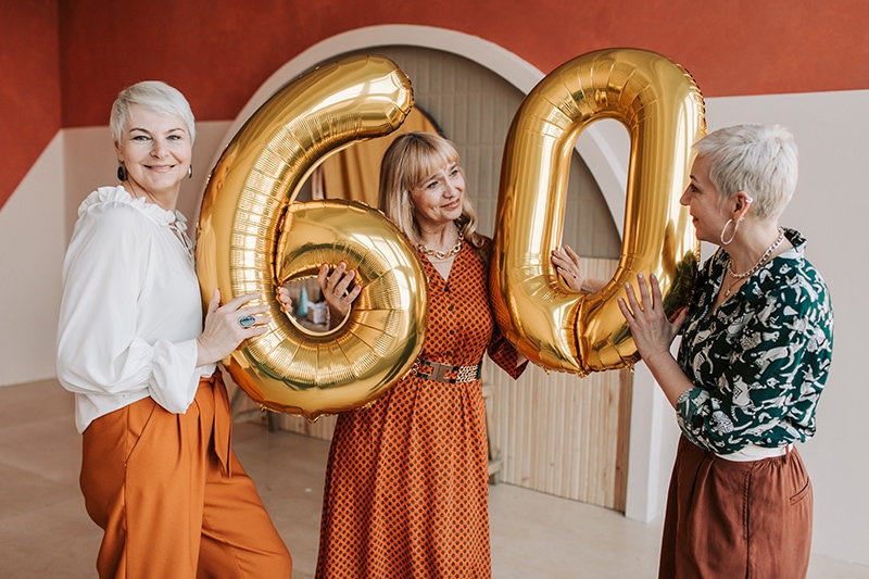 Drei ältere Freundinnen halten Luftballons zum 60. Geburtstag