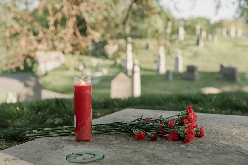 rote Blumen und rote Kerze auf einem Grab auf dem Friedhof