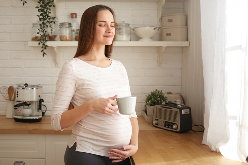 Schwangere Frau hält weiße Tasse mit geschlossenen Augen