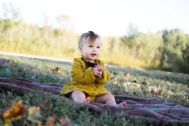 süßes Baby im gelben Kleid sitzt auf der Decke im Park