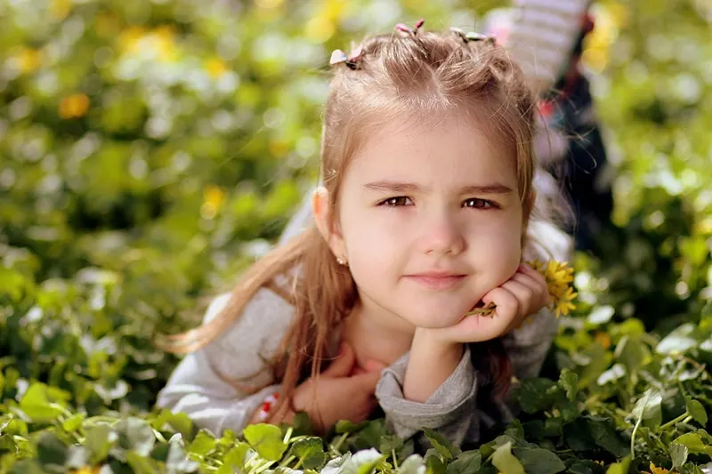 süßes kleines Mädchen, das auf dem Gras liegt und Blumen hält