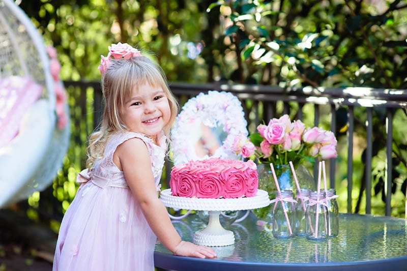 süßes kleines Mädchen posiert mit Kuchen auf ihrer Geburtstagsfeier