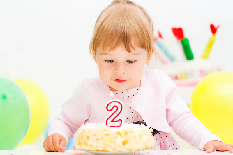süßes kleines Mädchen schaut auf Geburtstagskerze auf Kuchen