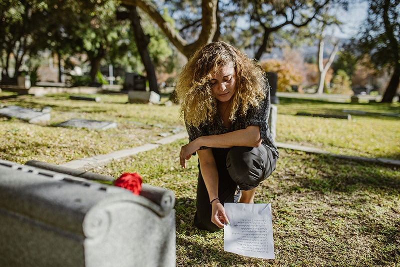 traurige Frau in der Nähe des Grabes, die einen Brief hält