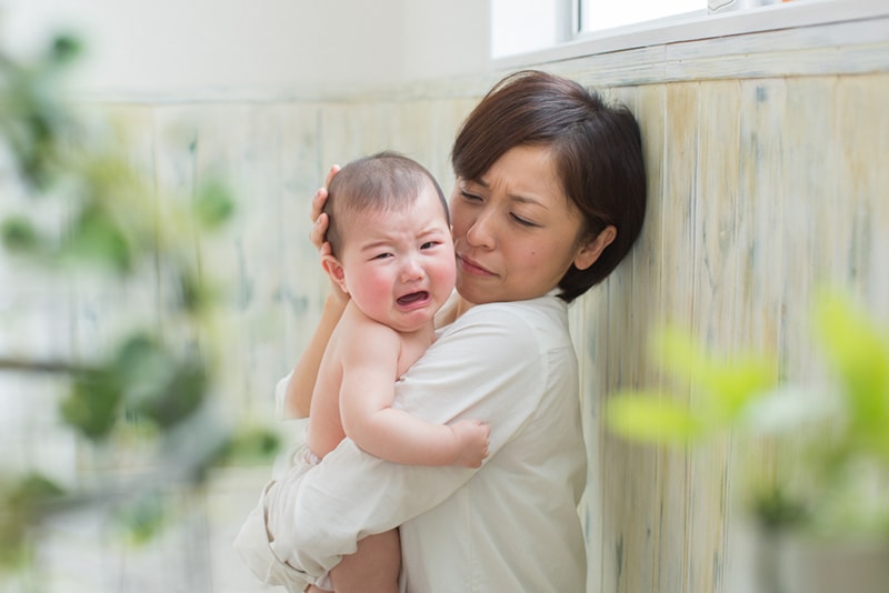 traurige Mutter, die ihr weinendes Baby tröstet, während sie sie in den Armen hält