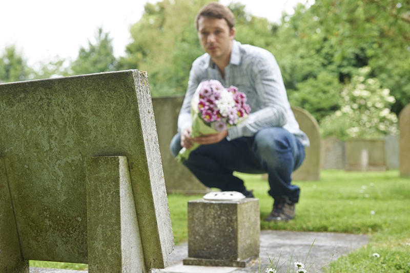 trauriger Mann, der im Grab kniet und Blumen legt