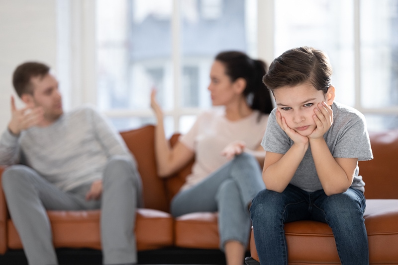 trauriger kleiner Junge, der vor den Eltern sitzt und sich hinter ihm auf der Couch streitet