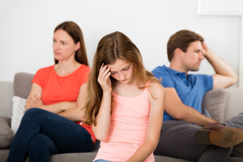 Trauriges Teenager-Mädchen, das vor Eltern sitzt, die sich hinter ihr streiten