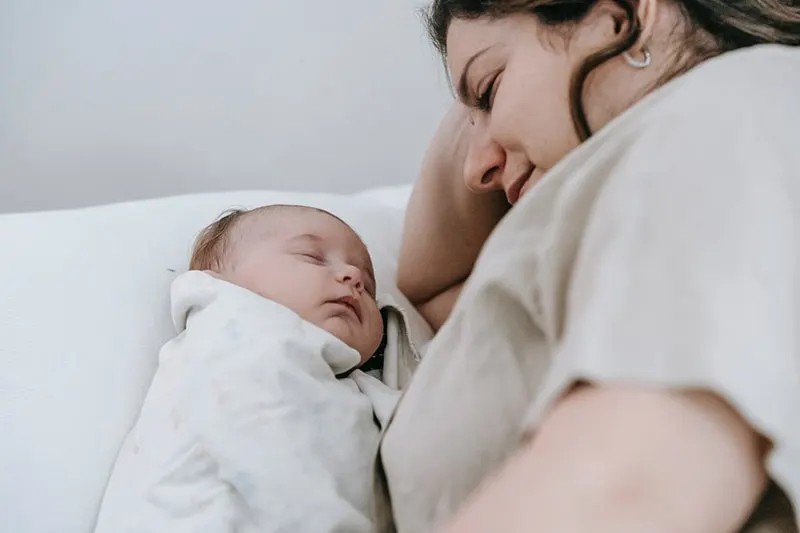 zufriedene Mutter, die schlafendes Baby auf dem Bett betrachtet