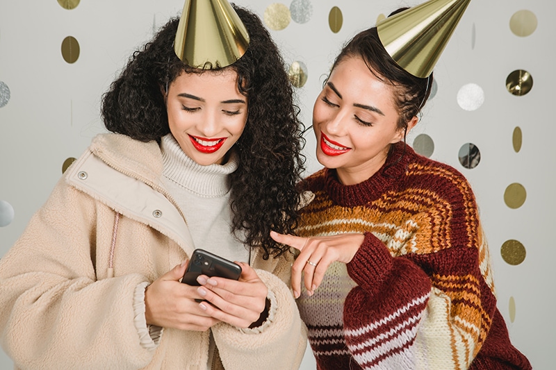 Zwei fröhliche Freundinnen, die auf der Geburtstagsfeier auf das Smartphone schauen