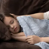Mama bedeckt verschlafenes Kind mit Decke