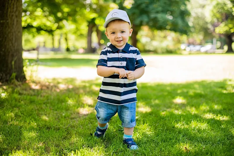 Baby mit Mütze steht auf dem Gras